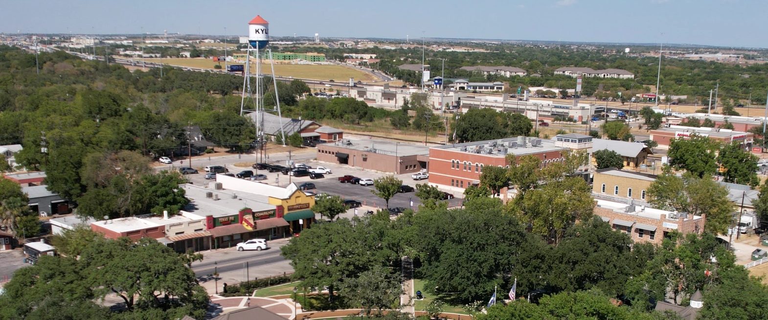 Aerial view of downtown Kyle, Texas: City Square Park and its live oaks, the brick storefronts on Center Street, and the Kyle water tower